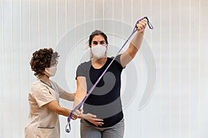 A pregnant woman exercising with an elastic band with help of physiotherapist