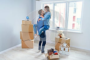 Front view of pretty smiling girl which holds by her handsome young boyfriend in the middle of their new flat full of