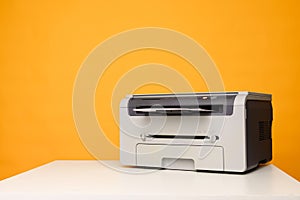 Front view of a printer and a blank sheet of a4 paper on a white table on a yellow background