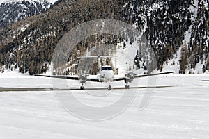 A front view of a private jet ready to take off in the snow covered landscape and mountains in hte alps switzerland in winter