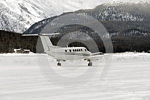 A front view of a private jet ready to take off in the snow covered landscape and mountains in hte alps switzerland in winter