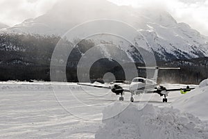 A front view of a private jet ready to take off in the snow covered landscape and mountains in hte alps switzerland in winter