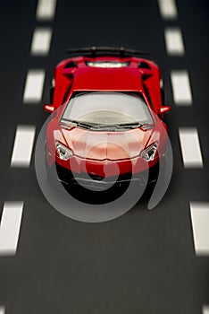 Front view of a red sports car on an asphalt background with road lanes