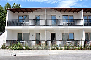 Front view of row of newly built motel room balconies with black metal fences and outdoor furniture surrounded with garden plants