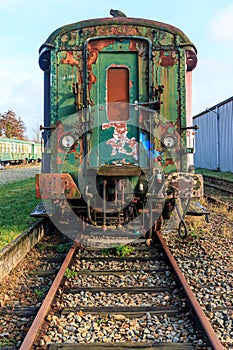 Front view of rusty and corroded green metal freight car on disused train tracks