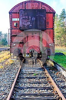 Front view of a rusty red metal freight car on disused train tracks at old station