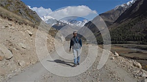 Front view of senior man hiker traveler tourist walking alone on mountain road in the summer while hiking enjoying nature. Travel