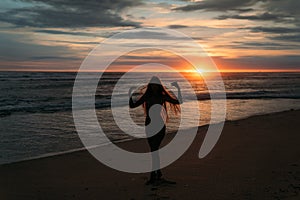Front view silhouette of attractive woman. Beautiful young girl with long hair walking on the beach, posing at sunset