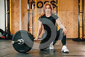 Front view. Sitting, barbell on the floor. Beautiful strong woman is in the gym