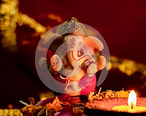 Front view of small ganesha statue and clay lamp against blurred red golden chunari in the background. hinduism concept