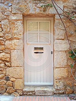 Front view of small white wooden door with metal mailbox and stone lintel. Stone lintel above rustic painted closed door.