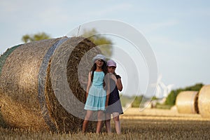Front view of smiling caucasian little girls hugging and looking at camera with fresh hay bales on farm. Modern