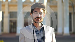 Front view smiling Middle Eastern man posing in sunshine on urban city street. Medium shot portrait of confident young