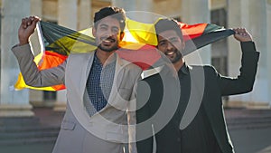 Front view smiling Middle Eastern men looking at camera standing with German flag outdoors. Positive confident young