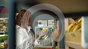 Front view of smiling young woman choosing lemons at grocery store picks up at fruit and vegetable aisle in supermarket.