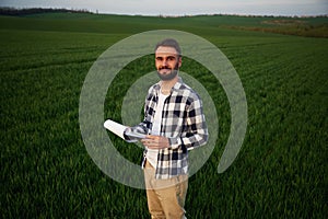 Front view. Standing and holding notepad with document. Handsome young man is on agricultural field