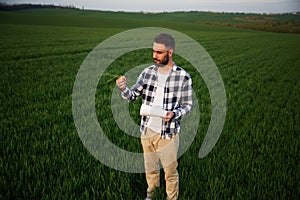 Front view. Standing and holding notepad with document. Handsome young man is on agricultural field