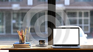 Stylish workplace with computer laptop, coffee cup, books and stationery on wooden table.