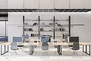 Front view on stylish workplaces and wooden book shelf in modern interior design open space office with white wall and glossy
