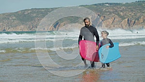 Front view of surf coach with disability and kid entering ocean