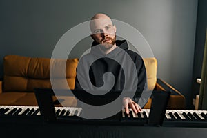 Front view of talented bald musician male with beard playing electric piano or digital synthesizer, practicing and photo