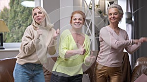 front view three cheerful adult women dancing simultaneously smiling looking at camera. Medium shot of joyful Caucasian