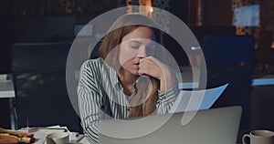 Front view of tired woman office worker reading documents and feeling sleepy. Young businesswoman working late at night