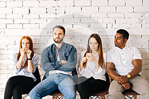 Front view of tired young diverse multi-ethnic job candidates in casual clothes waiting interview with hr, sitting in