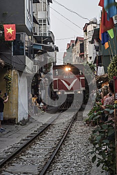 Train goes through a tiny street with locals and tourists in Ha Noi, Viet Nam