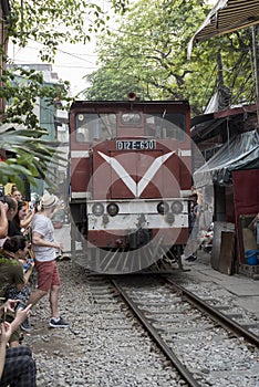 Train goes through a tiny street with locals and tourists in Ha Noi, Viet Nam