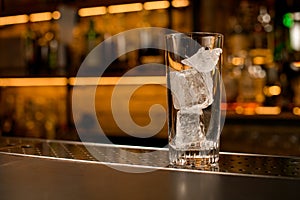 front view of transparent cocktail glass with ice cubes on bar counter
