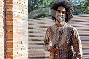 Front view of a cool young smiling afro man using a mobile phone while standing outdoors in a sunny day