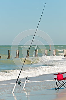 Front view of a tropical beach surf zone and two surf fishing rods in holders and a red beach chair