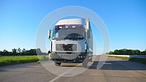 Front view of truck with cargo trailer driving on highway transporting goods at summer day. White lorry riding through