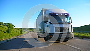 Front view of truck with cargo trailer speeding on highway and transporting goods at sunny day. White lorry riding