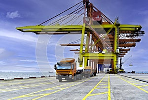 Front view of truck fleet line up under quay crane leaving the port after discharging containers with sea and blue sky background.