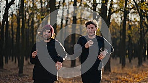 Front view of two brunette guys in black sportswear running and stopping during their morning jog in a sunny autumn park