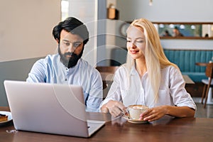 Front view of two business people of bearded Indian man and attractive Caucasian blonde woman working with laptop in