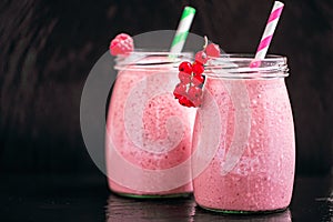 Front view of two jars with yogurt pink smoothie with cranberry, raspberry on black background.