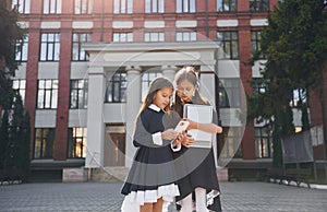 Front view. Two schoolgirls is outside together near school building