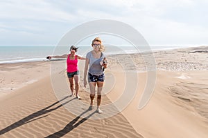 Front view of two women walking on top of a large dune, one of them with arms open to the wind. Mother and daughter