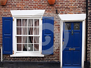 front view of a typical old small english terraced brick house with blue painted door and shutters
