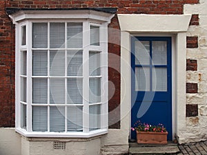 front view of a typical old small english terraced brick house with blue painted door white bay windows
