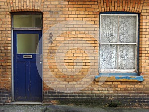 front view of a typical old small english terraced brick house with blue painted door and window