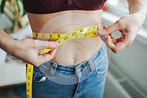 Front view of unrecognizable woman girl measuring her waist circumference with a tape measure.