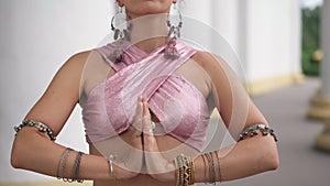 Front view unrecognizable woman in pink top with clasped hands standing at background of white columns. Slim performer
