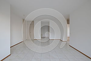Front view of a very bright living room with white walls. In the background you can see a built-in wardrobe and the entrance to
