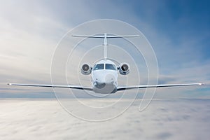 Front view of the white business jet flies in the air above the clouds