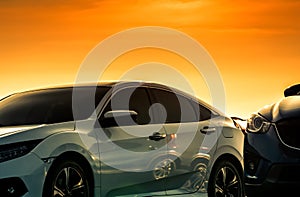 Front view of white car with luxury and modern design parked at parking lot with beautiful orange and golden sunset sky. Auto