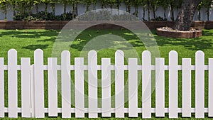 Front view of white wooden fence in front of artificial turf with green plant growing on interlocking brick blocks in front yard
